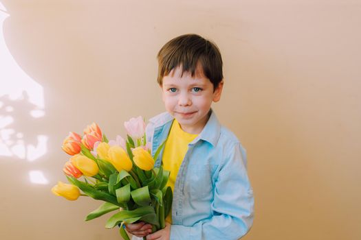 A boy with a bouquet of tulips lifestyle . Postcard for March 8. Congratulations on Women's Day. Congratulations on Mother's Day. Flowers are tulips. Baby and flowers
