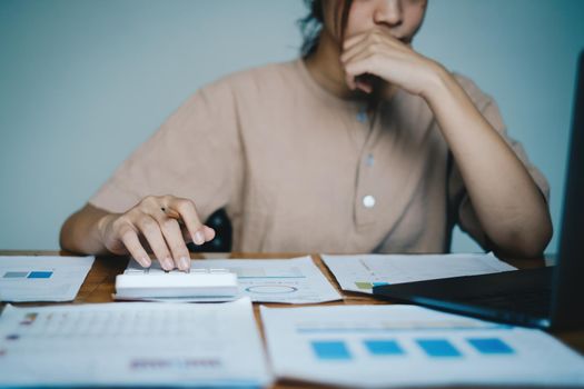 Asian Business woman or Accountant using calculator for audit finance budget on wooden desk in office, tax, accounting, statistics and analytic research concept