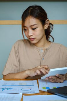 Asian Business woman or Accountant using calculator for audit finance budget on wooden desk in office, tax, accounting, statistics and analytic research concept