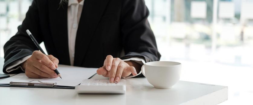 Crop shot of accountant woman hand press on calculator and writing a note for make financial report or company's profit annual at desk, bookkeeper job.