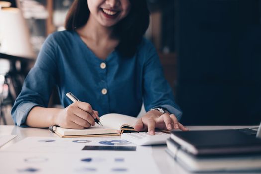 Asian Business Woman or Accountant hands holding pen writing in notebook with paperwork, account, audit and saving concept