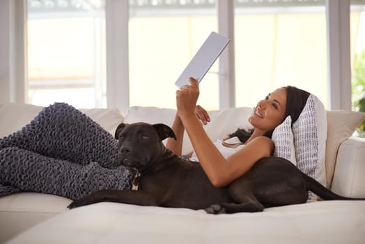 Shot of an attractive young woman relaxing on the sofa with her dog and using a digital tablet.