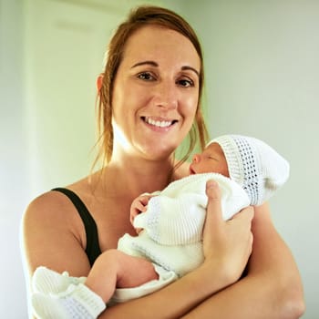 Portrait of cheerful young mother holding her infant son while looking into the camera at home.