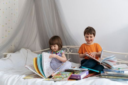 Two siblings reading books together on the sofa bed covered with white blanket in the kids' room