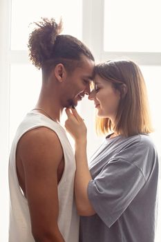 Portrait of a multiracial couple, boyfriend and girlfriend face to face, stand near the window.