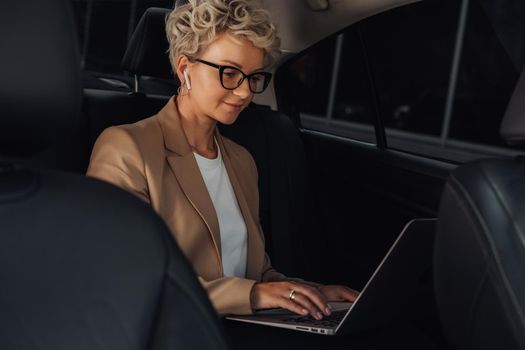 Stylish Business Woman Working on Laptop While Sitting on Back Seat of Car