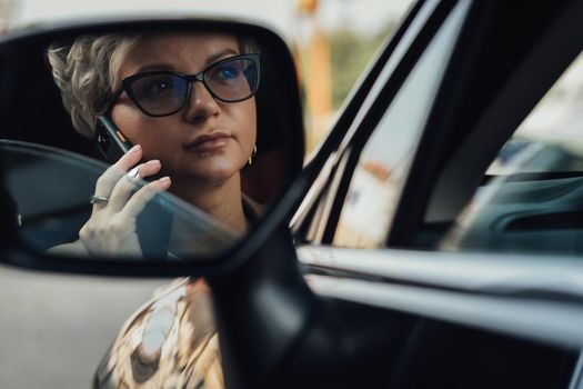 Stylish Woman in Glasses Talking on Phone While Driving Car, View Through Rear Mirror