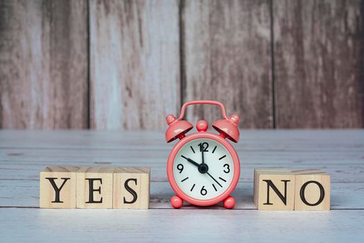 Yes No text on wooden block cube with alarm clock set at 10 o'clock on wooden background. Yes or No decision making. Choosing and answer.