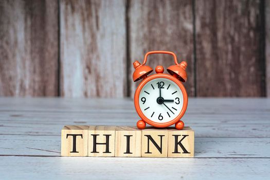 Think text on wooden blocks and alarm clock set at 3 o'clock on table. Business and idea concept.
