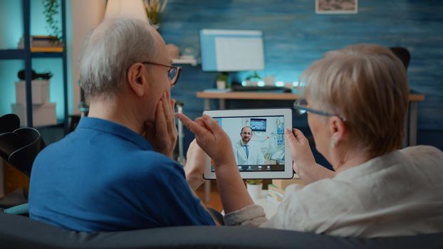 Aged man and woman talking to dentist on online video call, asking about toothache. Elder people using video teleconference to chat with orthodontist on digital tablet. Remote telemedicine