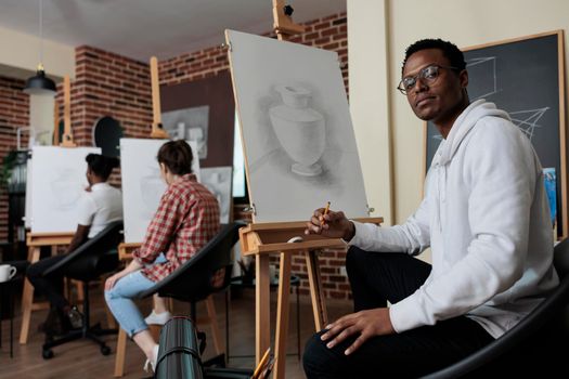 Portrait of smiling painter student attenting drawing class developing new artistic skill for personal growth. Diverse team sketching vase model working at graphic technique. Creative concept