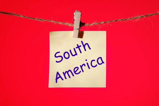 Phrase South America on a yellow sticker on a rope with clothespins on a red background..