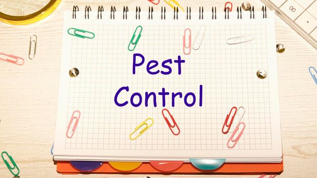 Pest Control text on a notebook in a cage with scattered paper clips on a notebook and a table.