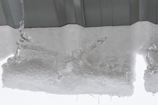 Icicles on the roof, white sky and iced water, winter ice