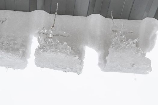 Icicles on the roof, white sky and iced water, winter ice