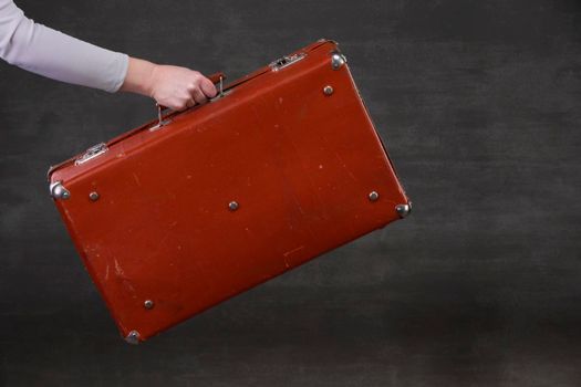 In hand is a brown retro suitcase on a gray background.