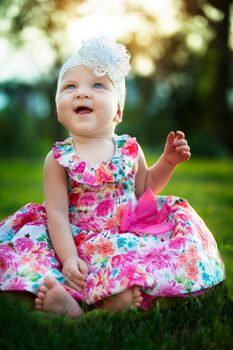 Happy little girl sits on the grass and laughs. Beautiful child. Little baby up to a year old on a summer meadow.