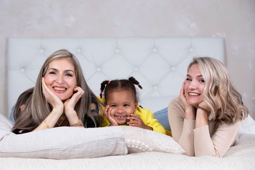 Family from different races. Mom grandmother light-skinned and a little African American girl lie on the sofa.