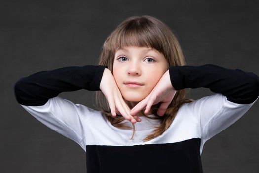 Beautiful little girl holding her face with her hands and looking at the camera.