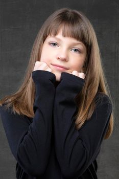 Portrait of a beautiful pensive girl of ten years old on a gray background.