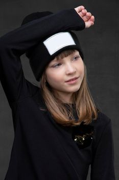 Portrait of a beautiful teenage girl in dark clothes on a gray background. Ten year old girl posing.
