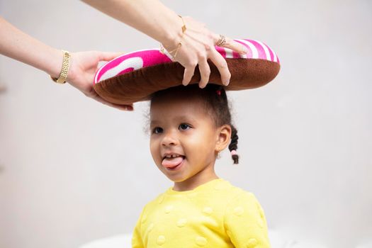 Mom's hands put a funny pillow on a little African girl.