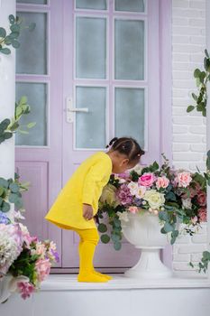 Little African girl in a yellow dress sniffs a bouquet of flowers near the purple door.
