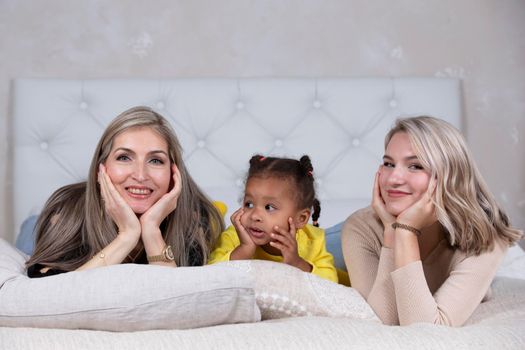 Family from different races. Mom grandmother light-skinned and a little African American girl lie on the sofa.