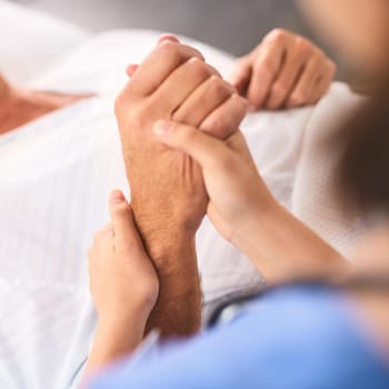 Closeup of a unrecognisable persons hand being held by a doctor inside a medical clinic.