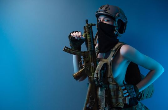 sexy girl soldier in a helmet, armed with an automatic rifle, in military clothes on a blue background