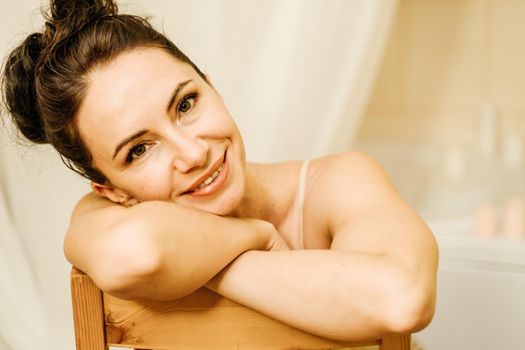 Portrait of a middle-aged woman, smiling with her arms folded in front of her face, her hair pulled up. The brunette is in a good mood. On a light background