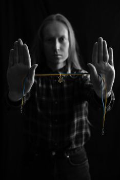 Ukrainian young blonde woman holding a pendant with the state emblem of Ukraine - Trident close up. Russia attacked Ukraine on February 24, 2022. Black and white vertical photo