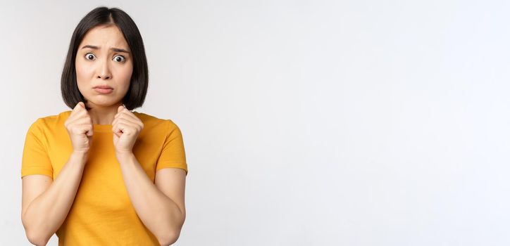 Portrait of scared asian woman shaking from fear, looking terrified and concerned, standing anxious against white background.