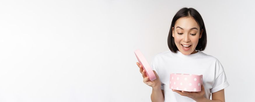 Happy asian woman, girlfriend open box with valentines day gift, receive romantic present, standing over white background. copy space