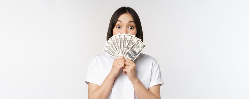 Happy asian girl holding money, cash near face, concept of microcredit and finance, white studio background. Copy space