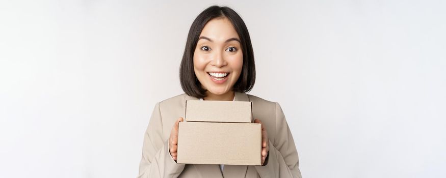 Enthusiastic asian businesswoman, giving customer order boxes, standing against white background. Copy space