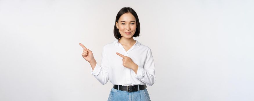 Image of smiling young office lady, asian business entrepreneur pointing fingers left, showing client info, chart of banner aside on copy space, white background.