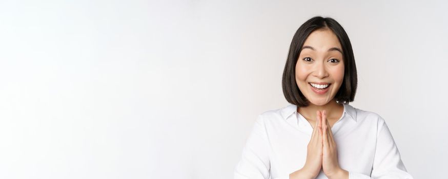 Close up portrait of young japanese woman showing namaste, thank you arigatou gesture, standing over white background.