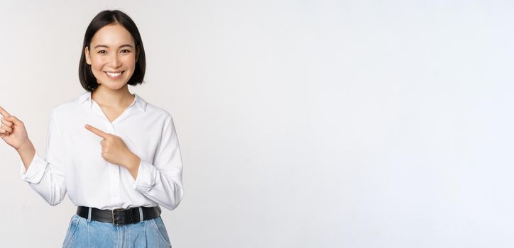 Image of smiling young office lady, asian business entrepreneur pointing fingers left, showing client info, chart of banner aside on copy space, white background.