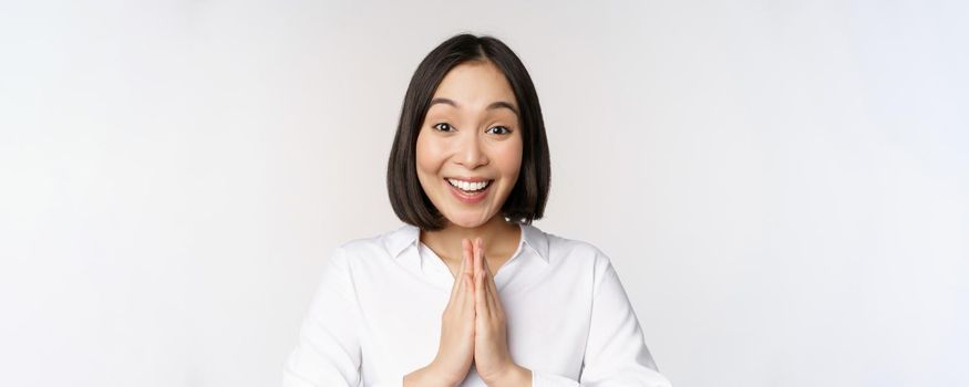 Close up portrait of young japanese woman showing namaste, thank you arigatou gesture, standing over white background.