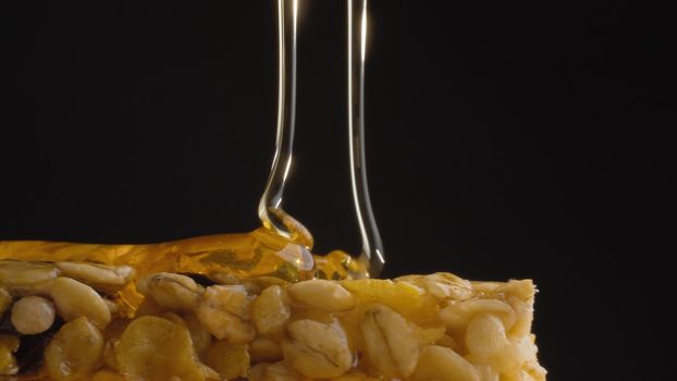 Extreme close up fresh honey pouring on a cereal bar, muesli on black background. Healthy energy fitness food