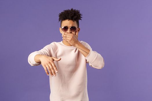 Waist-up portrait of cool and sassy, young carefree guy with dreads and sunglasses, cover mouth to beatbox, waving hand in rhythm music, singing rap or attend hip-hop party, purple background.