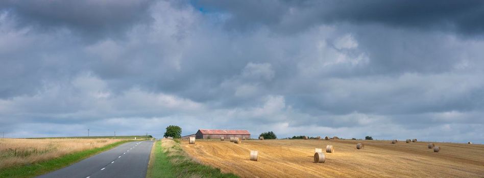 cloudy sky and summer countryside landscape with straw bales and barn in french ardennes near charleville
