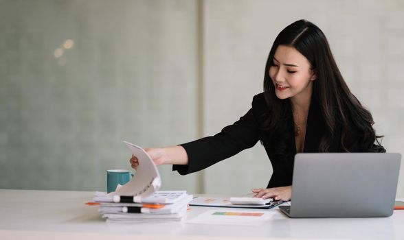 Charming asian business accountant woman working with computer and calculator for business and financial expense.