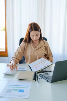 A female company employee is using a calculator to calculate sales income on a tablet computer screen via the Internet