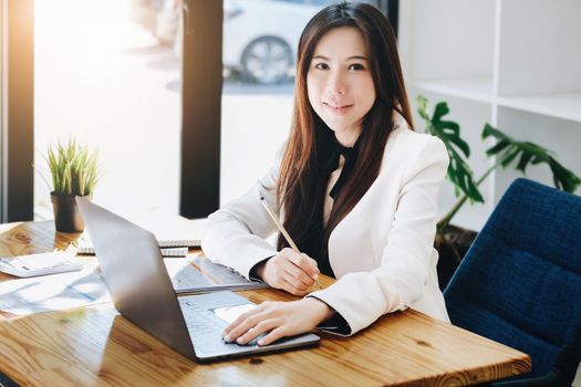 A female entrepreneur or businesswoman showing a smiling face while operating a computer working on a wooden table