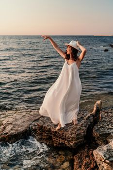 A woman in a white dress and hat is standing on the beach enjoying the sea. Happy summer holidays.