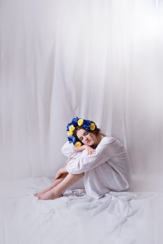 Beautiful Ukrainian woman in a white dress and floral wreath on white background . Symbol of the Ukrainian yellow blue flag. The calm lady is asleep. Peace in Ukraine