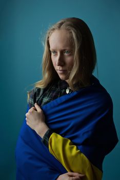 A real Ukrainian blonde woman during the war with the state yellow and blue Ukrainian flag on her head. Russia attacked Ukraine on February 24, 2022.