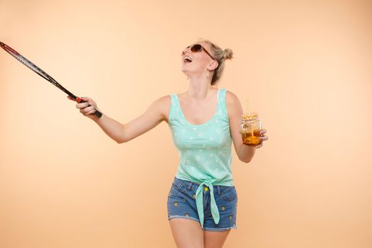 A woman in bright clothes, a T-shirt and denim shorts, sunglasses holds a ball and cold lemonade in her hands, on an isolated background.